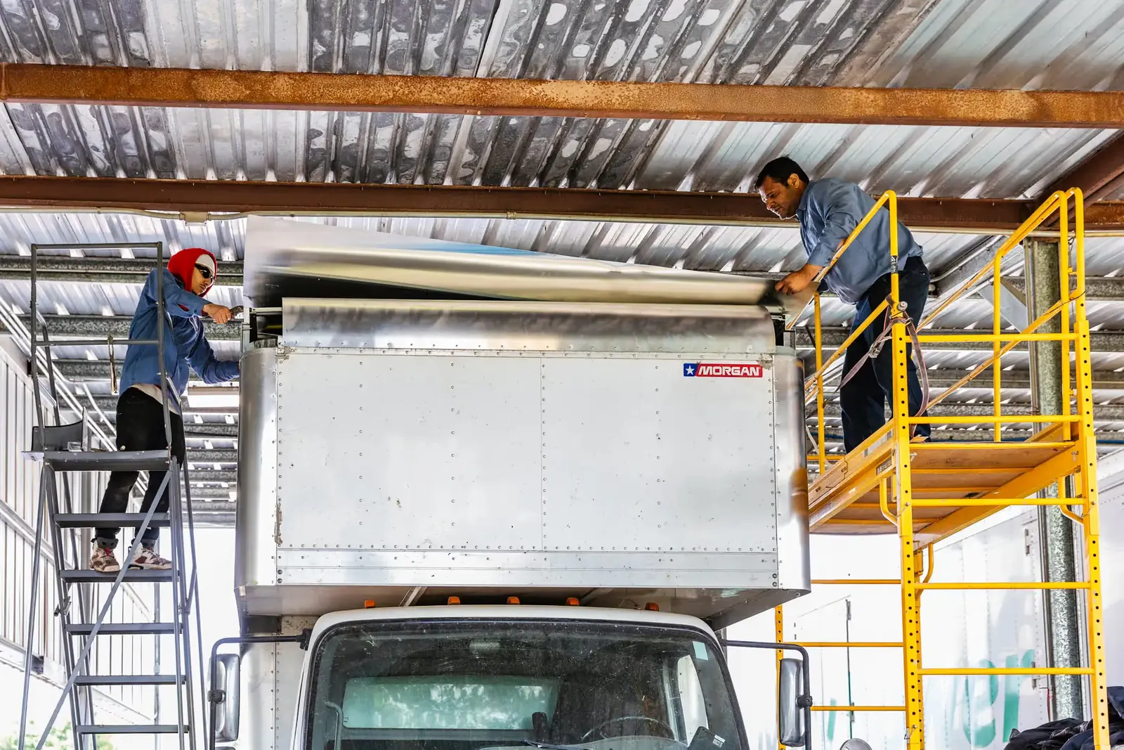 Technicians working on a box trailer on scaffolding